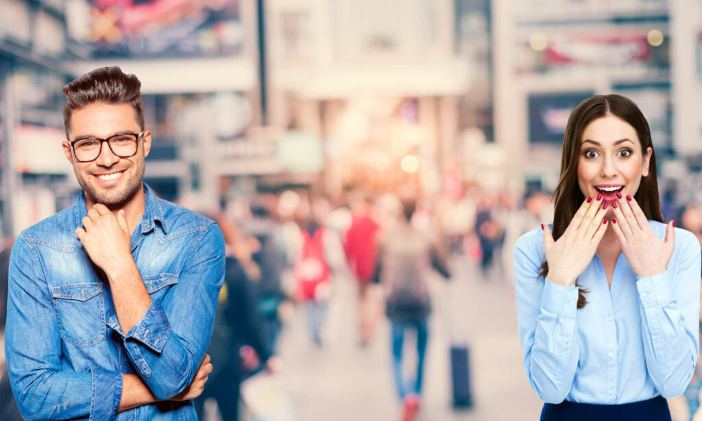 Ein Mann lächelt selbstbewusst mit der Hand am Kinn, während eine Frau mit den Händen vor dem Gesicht überrascht dreinschaut; beide stehen vor einer belebten städtischen Straßenszene, möglicherweise nach der Teilnahme an einem Caesar Sprachinstitut deutschkurs.